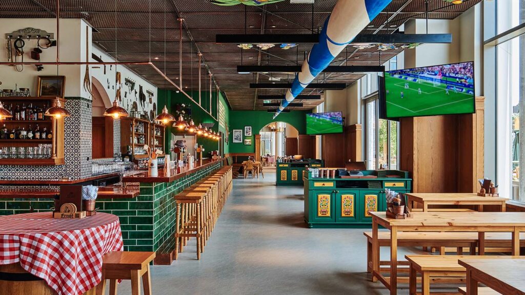 Inside Ernst Biergarten Dubai with a green-tiled bar, beer hall tables and sports screens