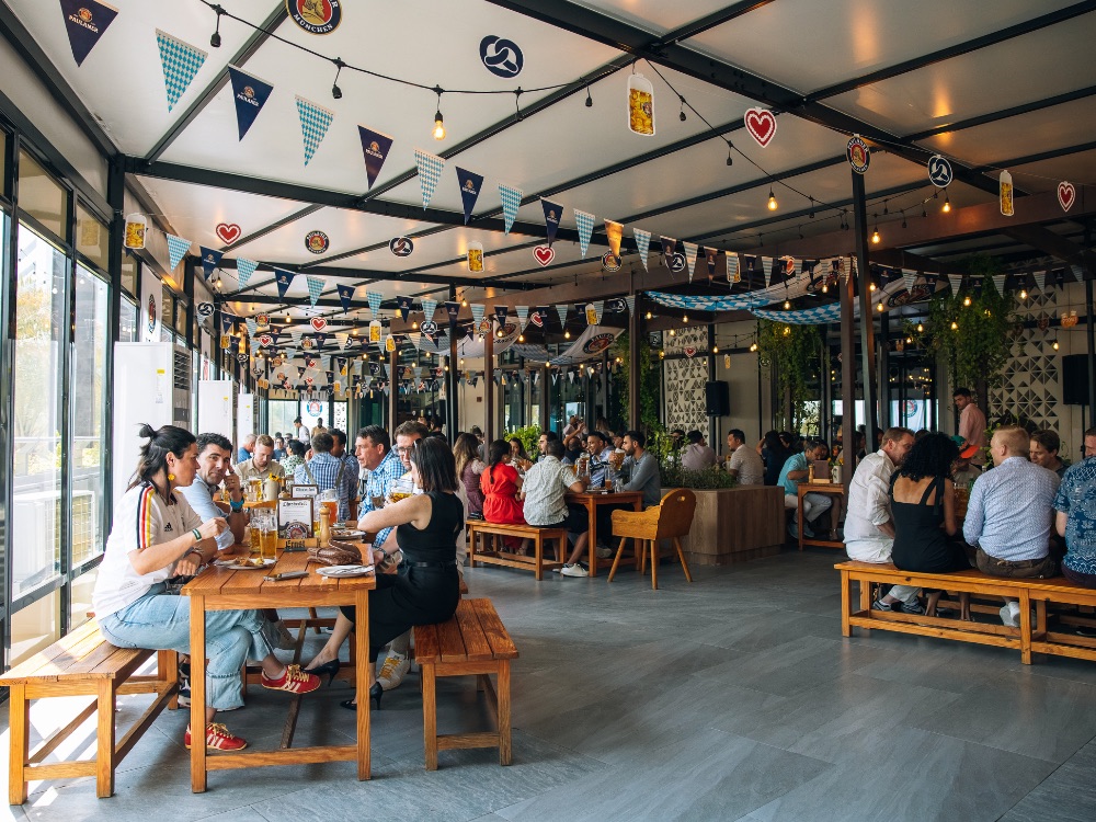 Guests at long wooden tables under Oktoberfest bunting at Ernst Biergarten Dubai