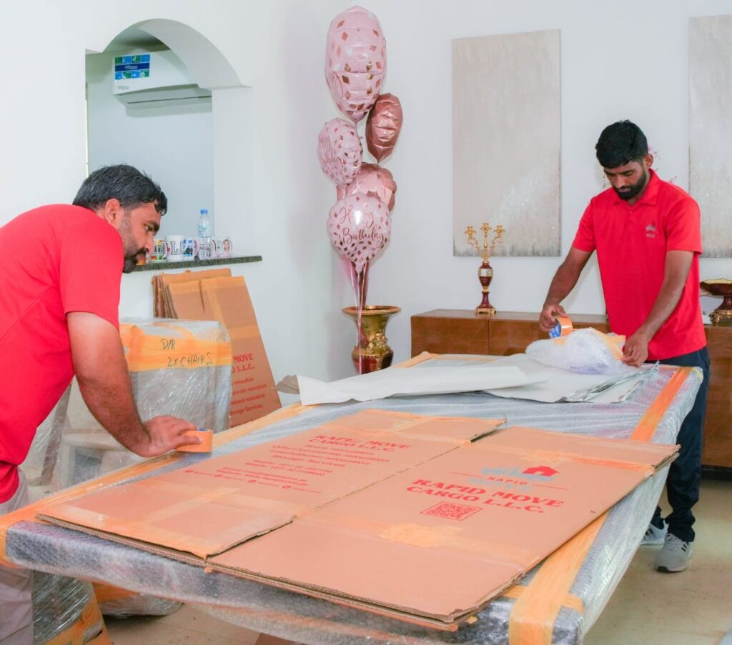 Movers wrapping a dining table with furniture labelled by room