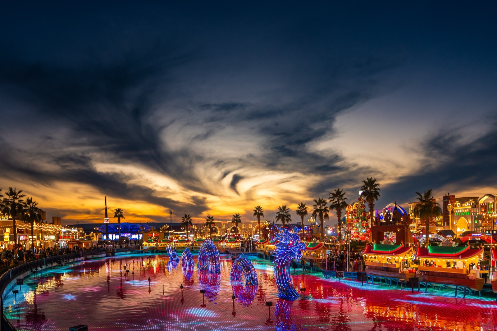 Global Village Dubai lake with a glowing dragon sculpture at sunset