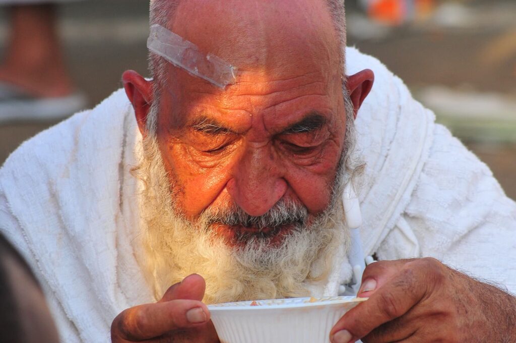 Elderly pilgrim in white ihram drinking from a cup during Hajj