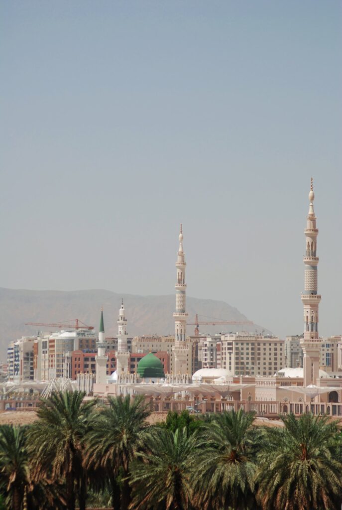 Minarets and green dome of Masjid an-Nabawi in Madinah behind palm trees